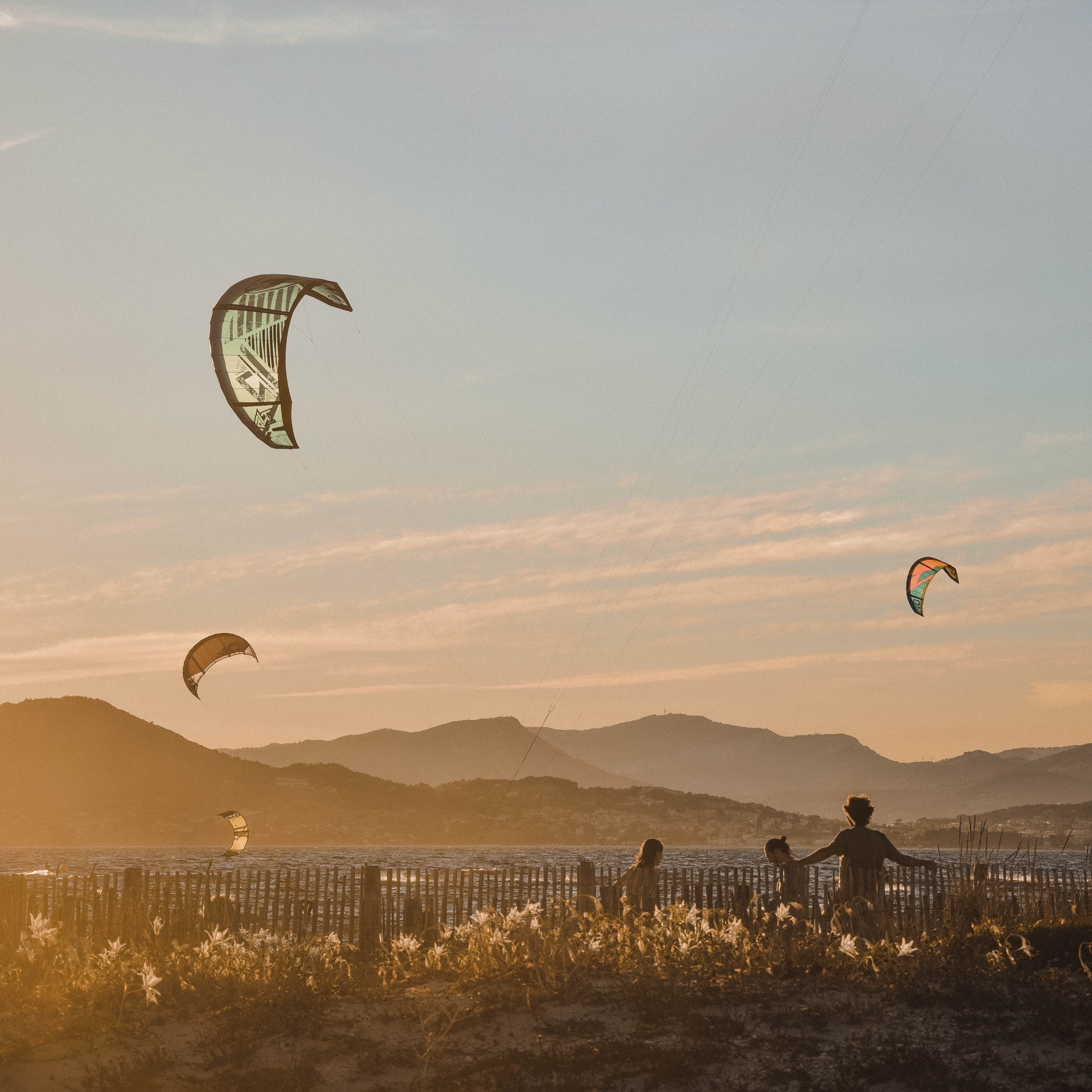 A family flies kites on a lakeshore at sunset.